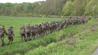 Soldaten laufen in einer langen Schlange über eine Wiese.