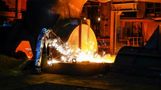 Ein Arbeiter in Schutzkleidung steht vor glühendem Stahl