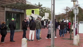 Menschen stehen in einer Schlange vor der Bremerhavener Stadthalle, um Tickets für das Spiel der Pinguins zu erhalten. 