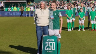 Werder-Fußballerin Michelle Ulbrich steht neben Abteilungsleiterin Birgit Brüggemann, die Ulbrich für 250 Bundesliga-Spiele geehrt hat.