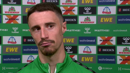 Werder-Kapitän Marco Friedl steht nachdenklich nach dem Spiel vor einer Werbewand beim Interview.