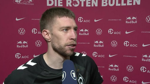 Werder-Profi Mitchell Weiser steht nach dem Spiel in Leipzig vor einer pinkfarbenen Werbewand beim Interview.
