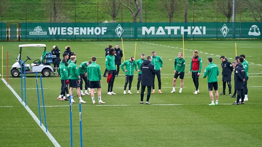 Werder-Spieler umringen auf dem Trainingsplatz ihren Trainer Ole Werner, der etwas erklärt.