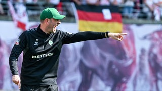Werder-Trainer Ole Werner ruft und deutet vehement an der Seitenlinie mit weit ausgestrecktem Arm seinen Spielern etwas an.