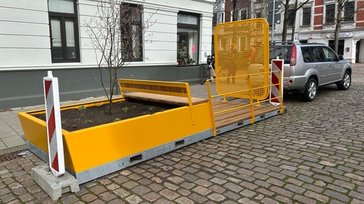 Eine gelbe Bank mit angeschlossenen Blumenkästen und einer Gitterwand vor dem Sichtfeld steht in Bremerhaven.