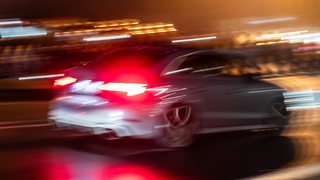 Ein Auto fährt bei Dunkelheit mit großer Geschwindigkeit über eine Straße.
