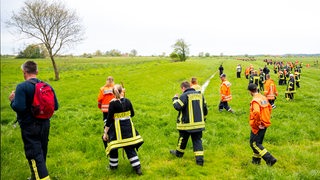 Feuerwehrleute suchen mit einer Menschenkette auf einem Feld nach einem vermissten Junge.