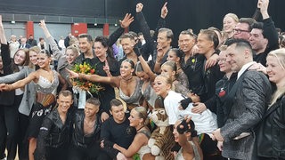 Die Tänzerinnen und Tänzer des Grün-Gold-Clubs mit Trainer Roberto Albanese jubeln beim Gruppenfoto nach dem Bundesligasieg.