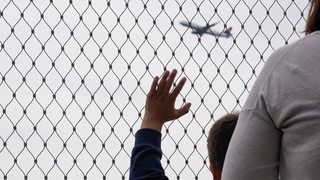 Junge winkt hinter Absperrgitter dem Flugzeug hinterher.