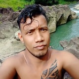 Ein Mann mit nacktem Oberkörper und Tattoo macht ein Selfie vor Felsen und Wasser.