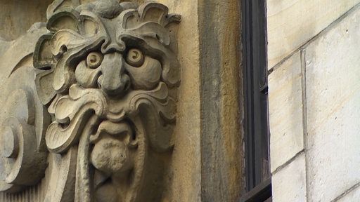 Ein Gesicht aus Stein ist an einer Fassade angebracht.