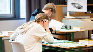 Schülerinnen und Schüler sitzen während einer schriftlichen Abiturprüfung in einem Klassenzimmer.
