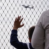 Junge winkt hinter Absperrgitter dem Flugzeug hinterher.