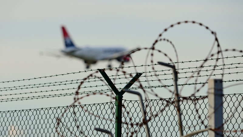 Ein Flugzeug hebt ab. Im Vordergrund ist Stacheldraht zu sehen.