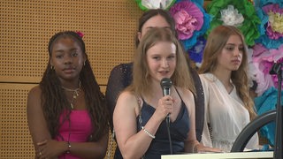 Vier Mädchen aus der zehnten Klasse stehen auf der Bühne. Ein Mädchen hat ein Mikrofon in der Hand und hält eine Rede.