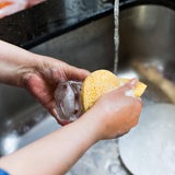 Zwei Hände spülen Geschirr in der Spüle.