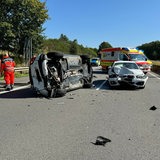 Nach einem Unfall auf einer Autobahn liegt ein schwerbeschädigtes Auto auf der Seite. 