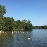 Blick von der Brücke, die über den Achterdieksee führt in Richtung des weiten Teils des Sees. Badende stehen versprenkelt im Wasser.