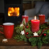 Ein Adventskranz mit Weihnachtsdekoration und roten Kerzen sowie eine Tasse Kaffee stehen auf einem Tisch vor dem Kamin in einem Wohnzimmer.