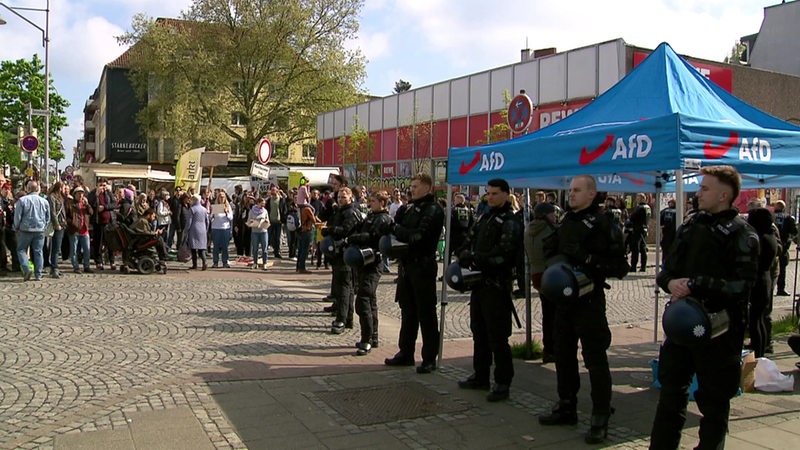 Vor einem Infostand der AfD stehen mehrere Polizisten.