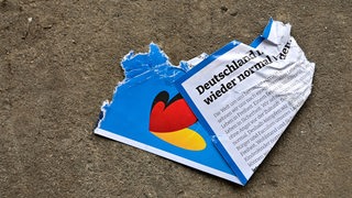 In einer Halle einer Entsorgungsfirma liegt auf dem Fußboden ein zerrissener AfD-Flyer aus dem Bundeswahlkampf.