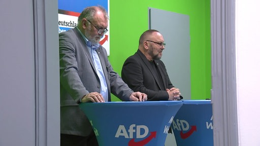Es sind zwei Politiker der AfD an Stehtischen zu sehen.