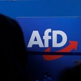 Delegierte gehen vor dem Parteilogo bei dem AfD-Bundesparteitag in Magdeburg. 