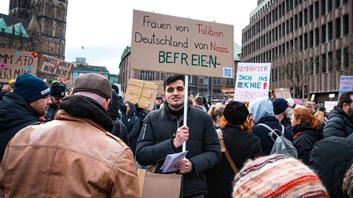 Auf einer Demonstration gegen Rechtsextremismus in Bremen hält ein junger Mann ein Schild mit der Aufschrift "Frauen von Taliban-Deutschland von Nazis befreien" in die Höhe.