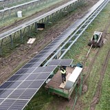 Arbeiter mit Landmaschinen setzen Solarzellen auf Metallgerüst