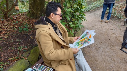Ein Mann sitzt auf einer Bank und schaut auf gemalte Bilder.