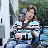 Eine dreißigjährige Frau mit braunen Haaren sitzt im Rollstuhl und schaut nach oben 
