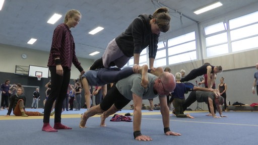 Artisten und Artistinnen in einer Turnhalle, die Akrobatik zusammen machen.