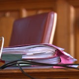 Ein Stapel rosafarbener Akten liegt auf einem Tisch in einem Gerichtssaal