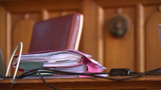 Ein Stapel rosafarbener Akten liegt auf einem Tisch in einem Gerichtssaal