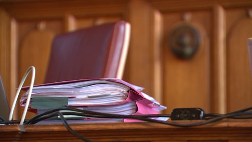 Ein Stapel rosafarbener Akten liegt auf einem Tisch in einem Gerichtssaal