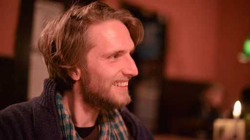 Lächelnder junger Mann mit Vollbart in rötlichem Kneipenlicht im Profil