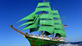 Ein Schiff mit grünen Segeln fährt über das Meer.