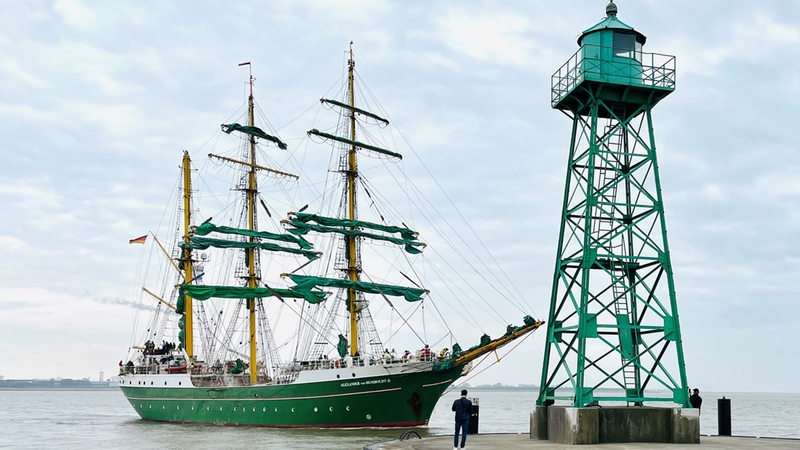 Ein Schiff mit grünen Segeln fährt auf eine Kaje zu. 