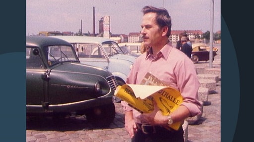 Ein altes Bild auf dem der Werkmeister Alfred Taake ist. Im Hintergrund stehen geparkte Autos.
