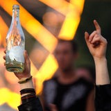 Zwei Hände zeigen in die Luft, eine davon hält eine leere Flasche Alkohol.