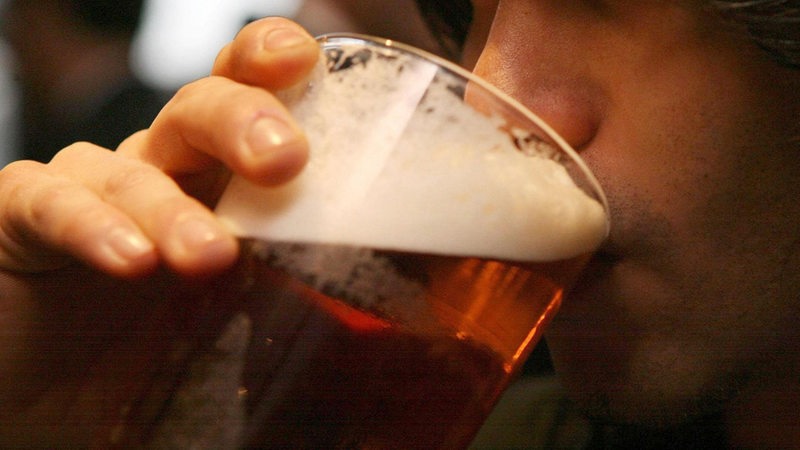 Nahaufnahme: Ein junger Mann trinkt aus einem Bierbecher.