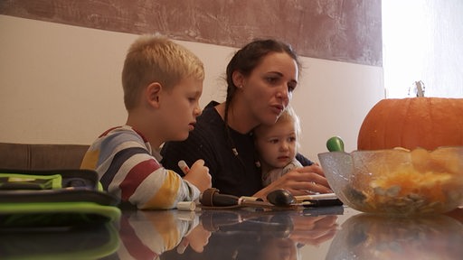Eine Frau sitzt mit ihren Kindern vor einem Kürbis.