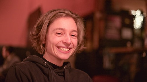 Junge Frau mit mittellangen Haaren lächelt in rötlichem Licht in Kamera
