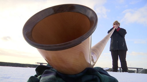 Eine Frau ganz klein hinter einem riesigen Alphorn Instrument.