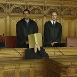 Der Angeklagte hält sich einen Aktenordner vor das Gesicht.