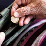 Die Hand einer älteren Frau hält eine Geldtasche, aus der sie ein 1-Euro-Stück nimmt.