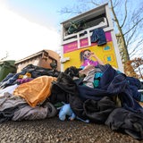 Gebrauchte Kleidungsstücke liegen vor einem Sammelcontainer für Altkleider