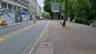 Die provisorische Fahrradstraße Am Wall in der Bremer Innenstadt. Auf der Autospur ist mit gelben Markierungen und Barken ein Bereich für Fahrradfahrer abgeteilt.