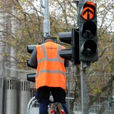 An einer Verkehrsampel führt ein Arbeiter mit Warnweste eine Reparatur aus.