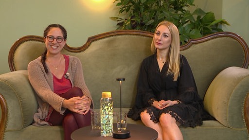 Zwei Frauen sitzen nebeneinander auf einem Sofa beim Interview. 